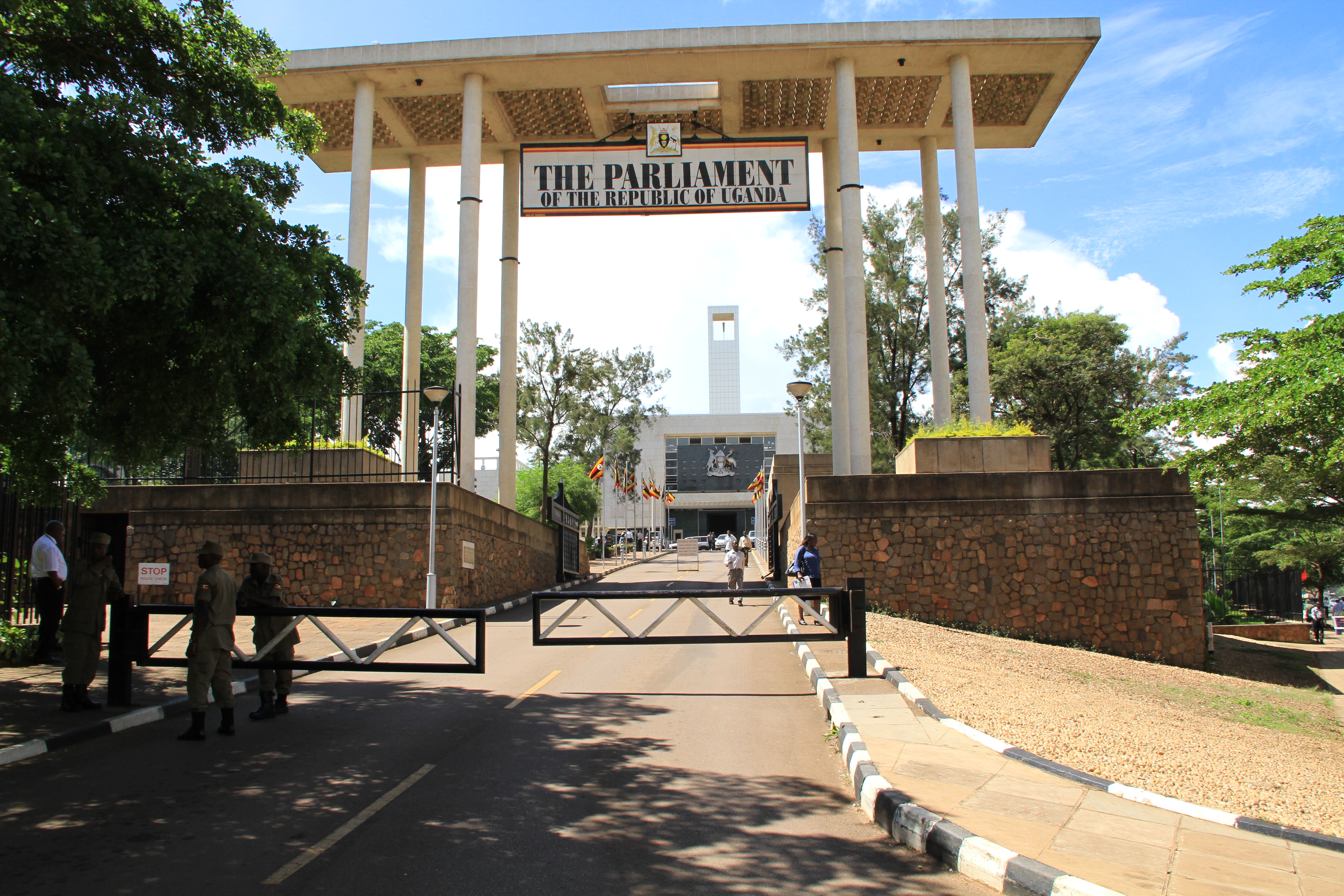 The entrance to the Parliament of Uganda. A gate and columns photographed in sunshine and surrounded by foliage.