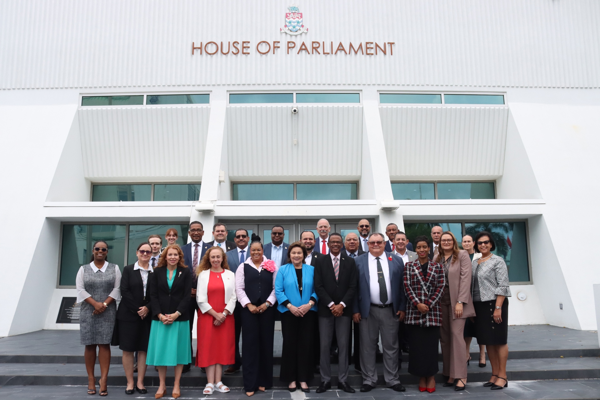 A group of people standing in front of the entrance of the Cayman Islands House of Parliaments.
